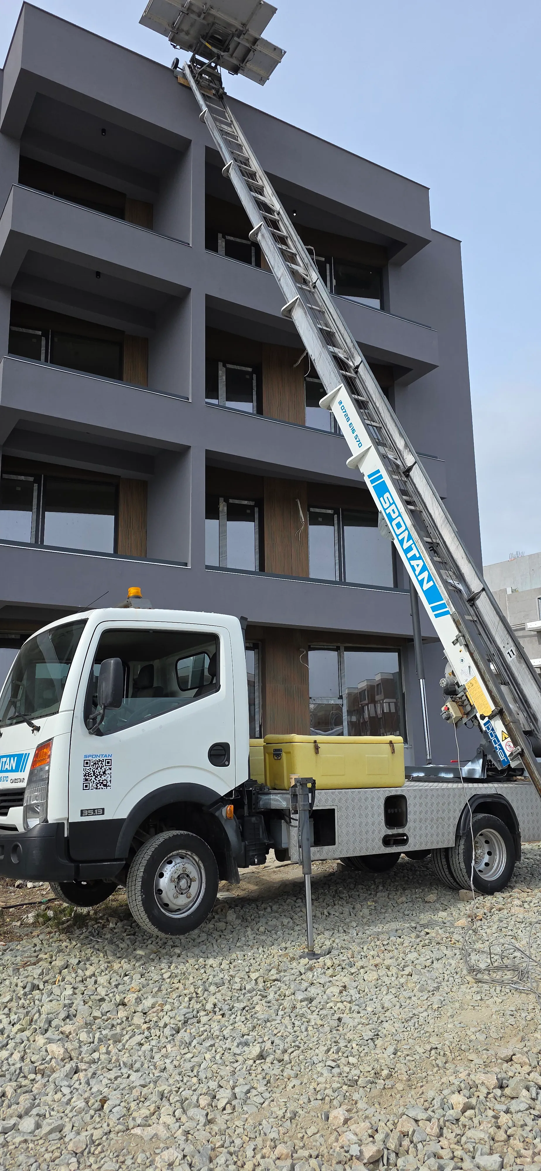 Camion cu lift exterior stabilizat pe teren lângă o clădire.