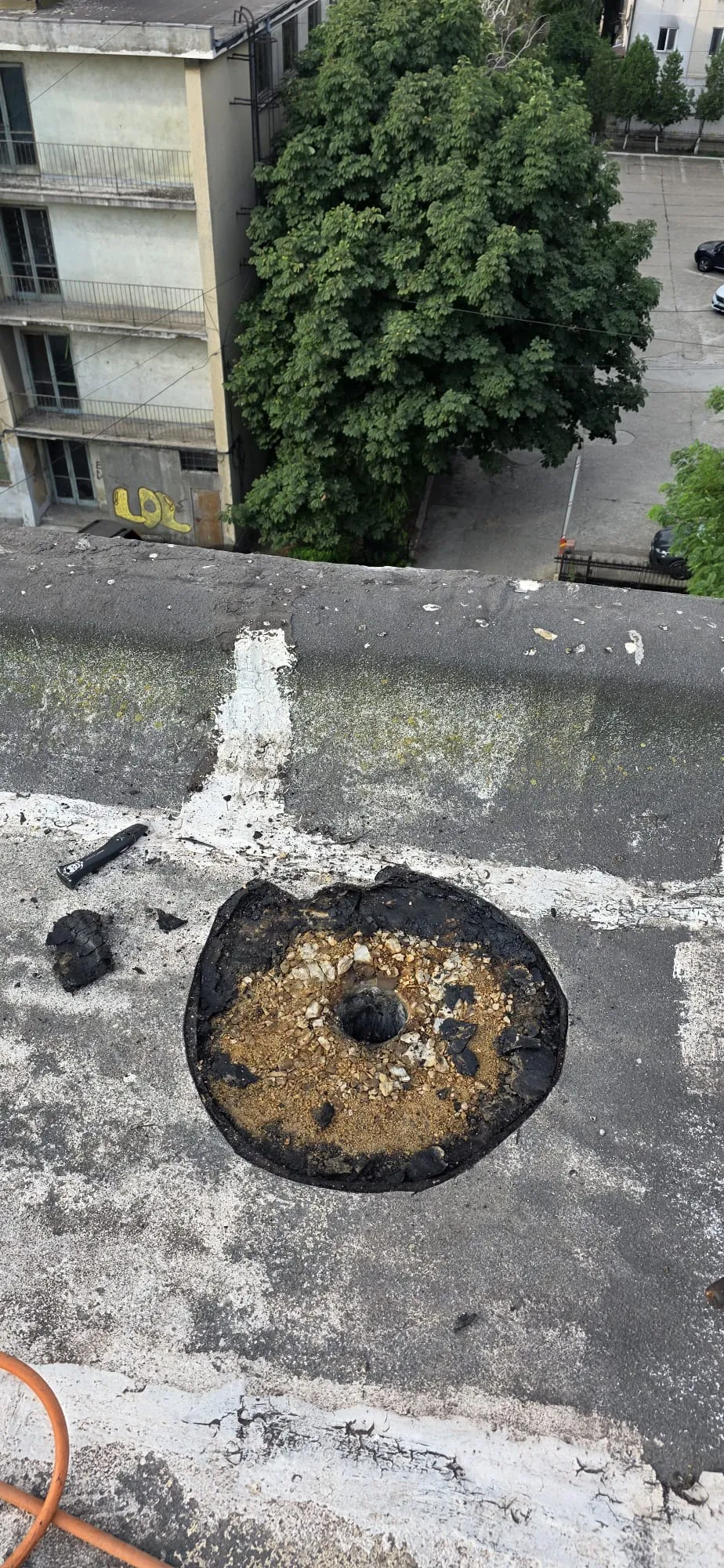 Zonă decopertată în jurul unei scurgeri de terasă, cu suportul expus și deschiderea tubului pluvial vizibilă.