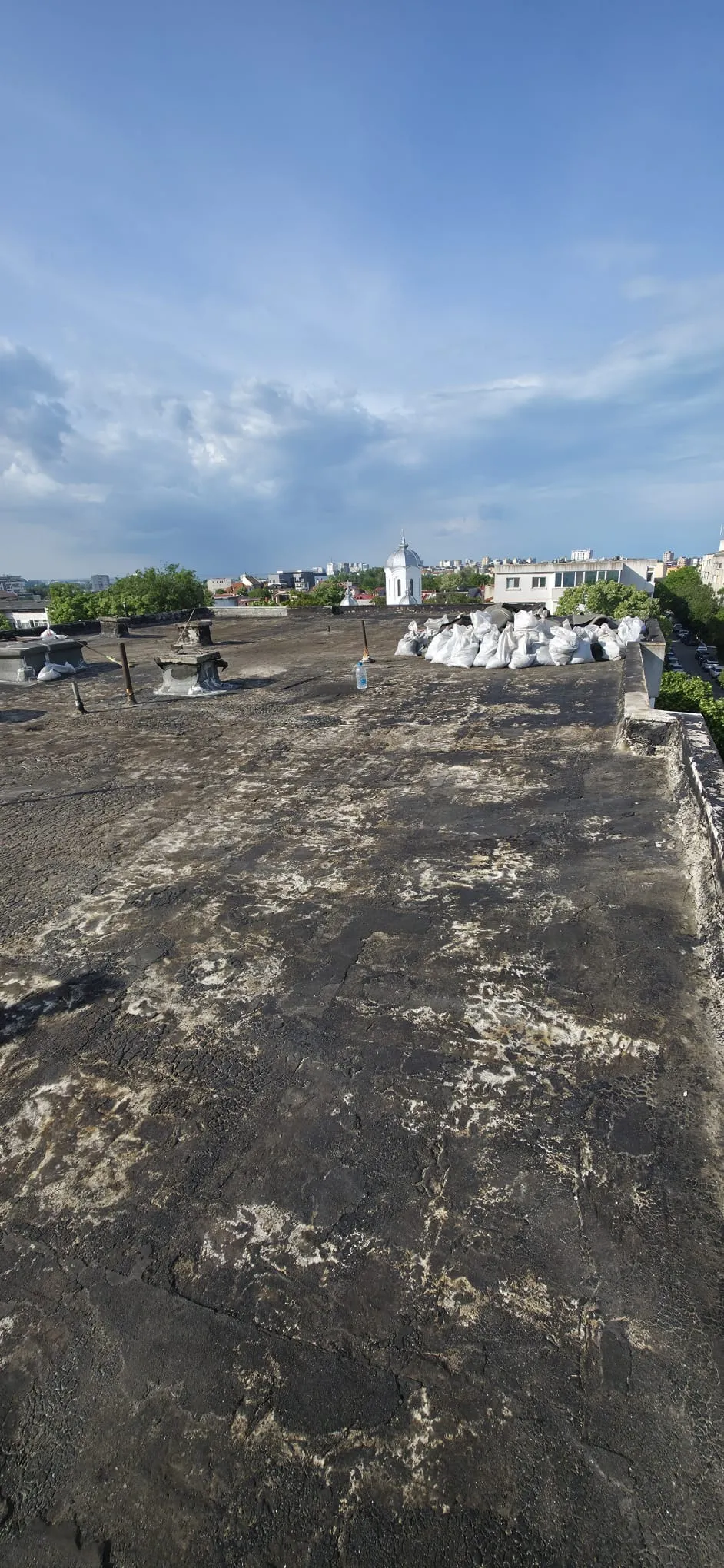 Terasă după îndepărtarea membranelor suprapuse, cu stratul bituminos vechi expus și saci cu materialele rezultate.